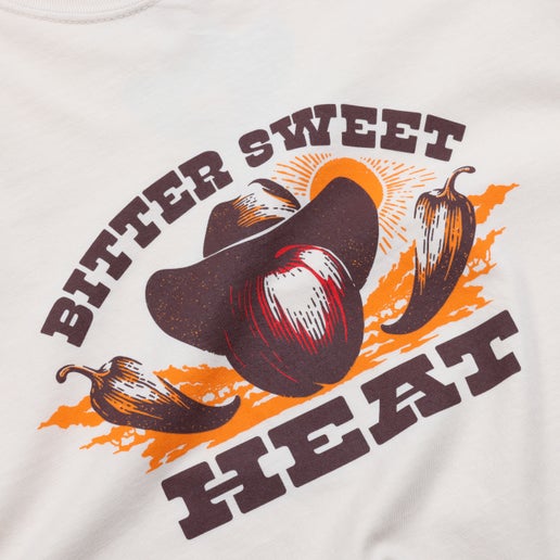 Close-up of the front of tee which displays an apple wearing a cowboy hat with a chili pepper on each side of it. The word "Bittersweet" is arched over the apple and below the apple is the word "HEAT".