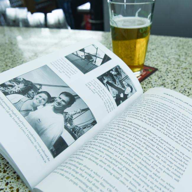 A copy of "Brewing Up A Busin" by J Wiley and Sons Publishing rests open on a speckled table beside a pint of beer, offering inspiration to homebrew enthusiasts. The softly blurred background adds to the inviting scene.