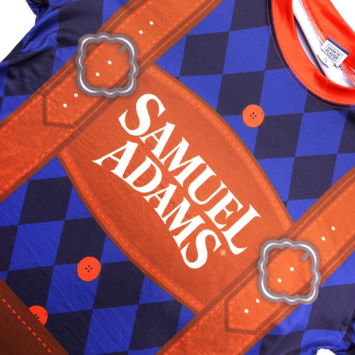 Close-up of front of lederhosen tee. Tee is blue checkered with orange lining around the neck and sleeves. Features imagery of suspenders and large writing "Samuel Adams" in the center.