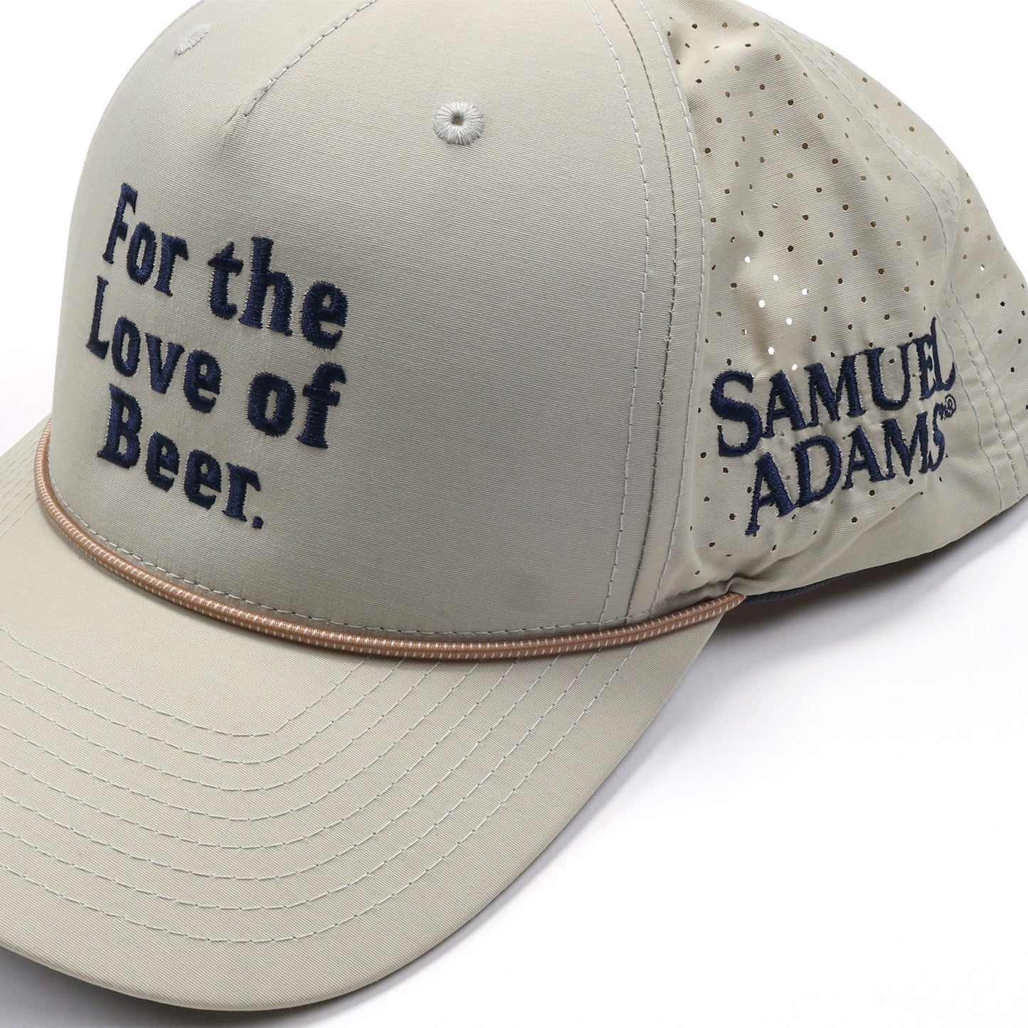 Close up of Oatmeal colored, navy embroidery Samuel Adams "For the Love of Beer" athletic hat. Left side view shows a Samuel Adams text logo in matching style. The hat features a rope lining the front two panels of the brim of the hat.