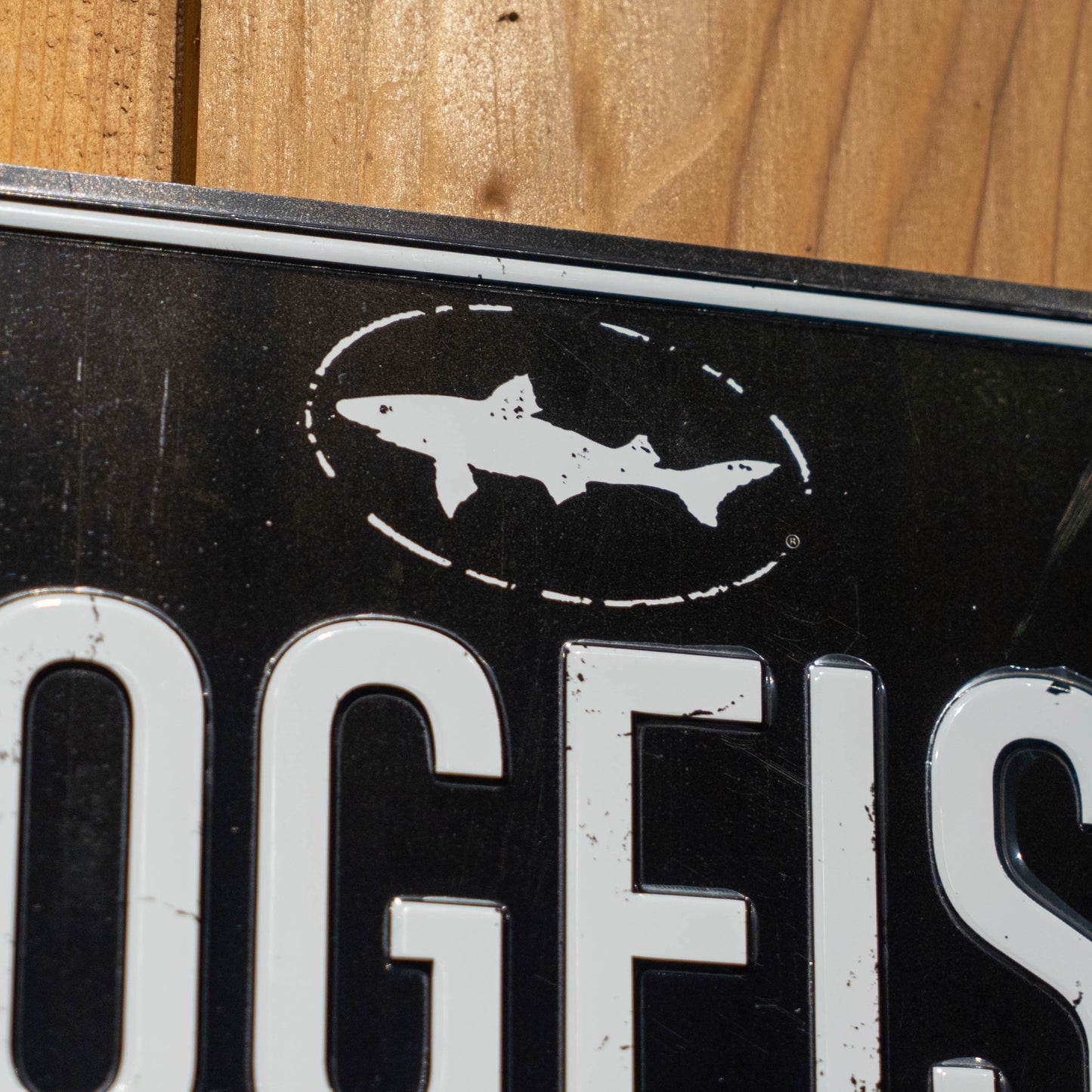 A close-up of the Black DOGFISH License Plate Tacker by Merchtank, featuring a white dogfish silhouette in an oval and white lettering—ideal wall décor for any Delaware beer lover.
