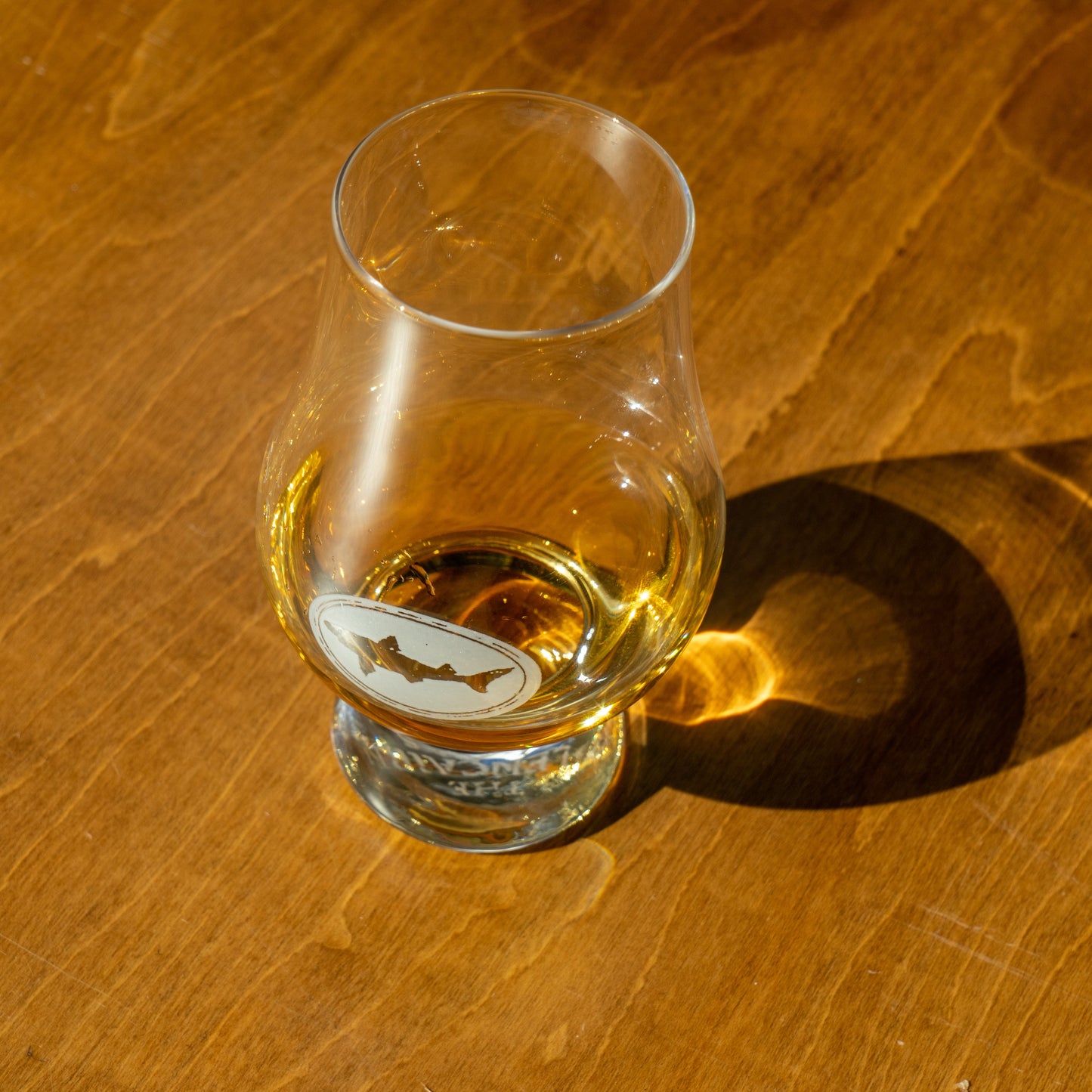 Dogfish Head Glencairn glass with etched shark logo, filled with golden colored dogfish IPA, shown on wooden tabletop