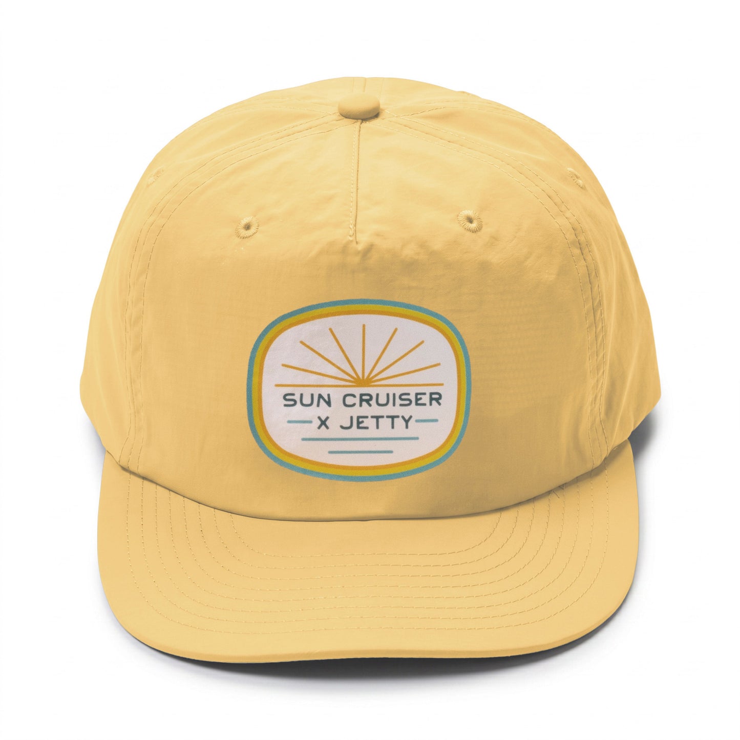 A yellow baseball cap featuring a circular embroidered patch on the front that reads 'SUN CRUISER X JETTY' with a sunburst design.