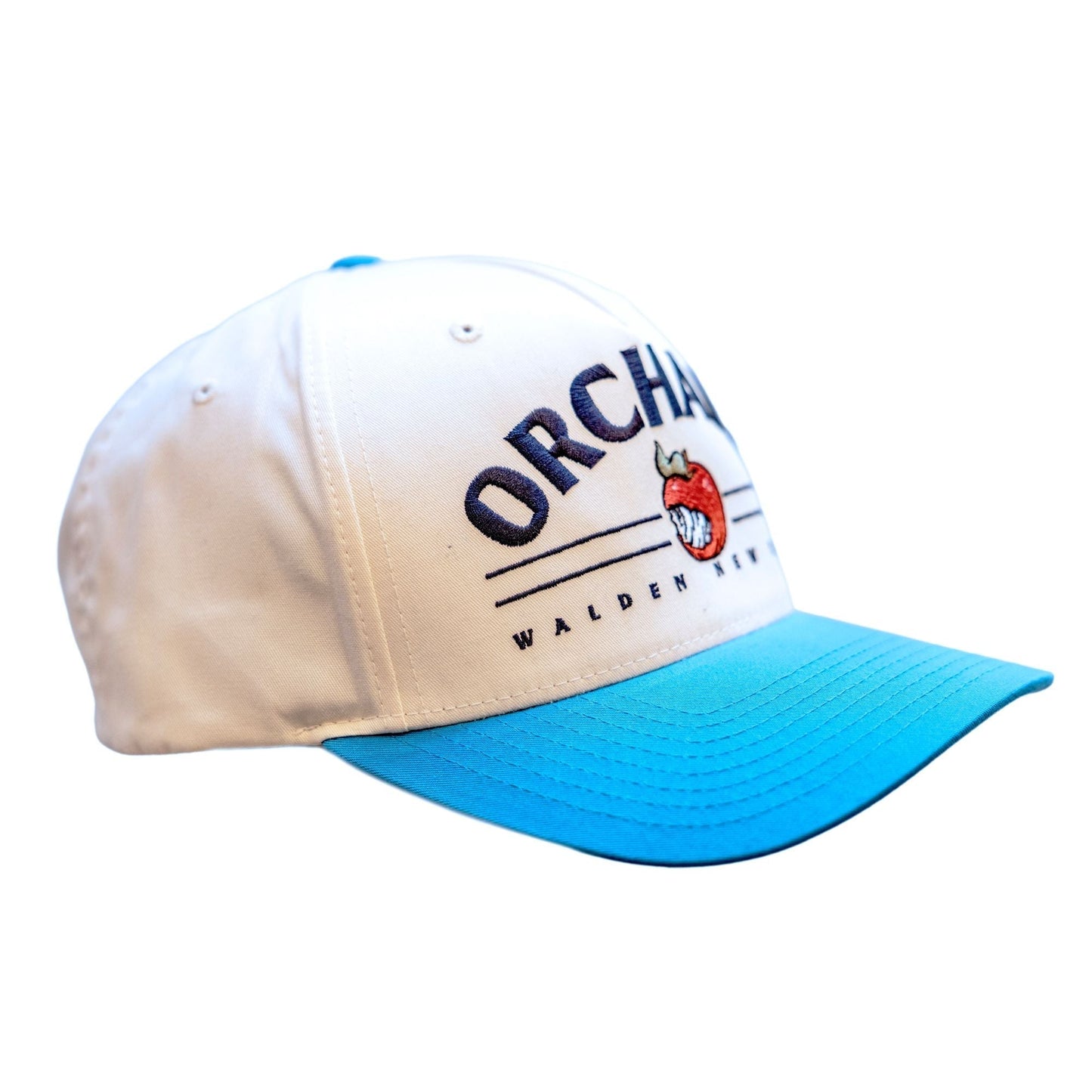 Side angle of the Vintage Five Panel Snapback. The Top button and brim are angry orchard blue. The 5 panels are white. On the front of the hat in large arching text reads "Orchard". Below this text are two thin, black horizontal parallel lines for design. An angry orchard apple logo breaks in the center of these lines. Underneath the lines in smaller black text reads "Walden New York"