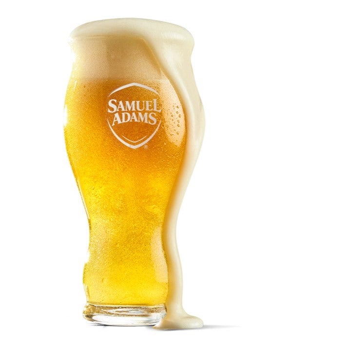 A 16oz pint glass filled with beer with the Samuel Adams classic shield logo printed on the front in white.