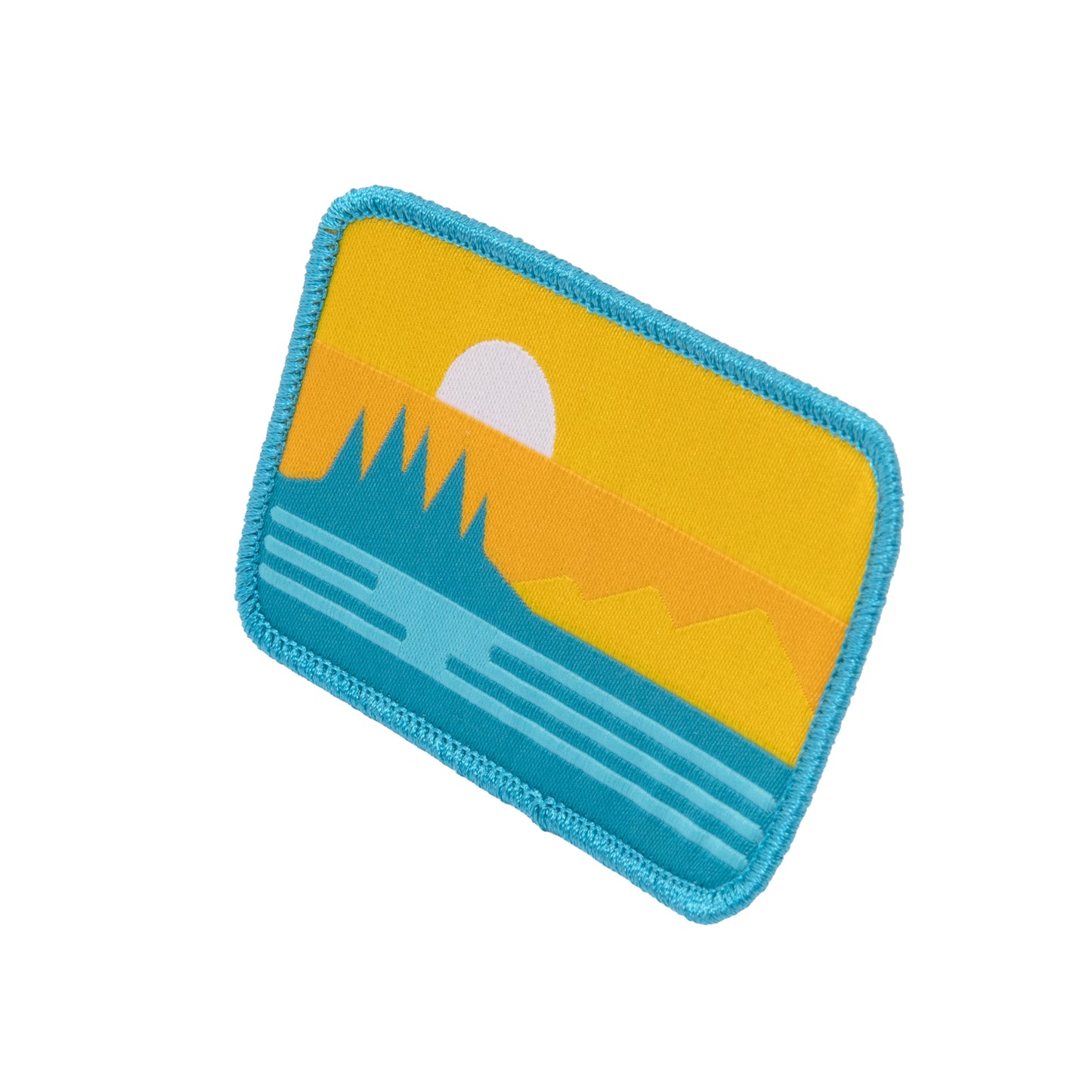 Close-up angled view of Sun Cruiser logo patch featuring yellow sunset, blue ocean waves, and retro mountain landscape design