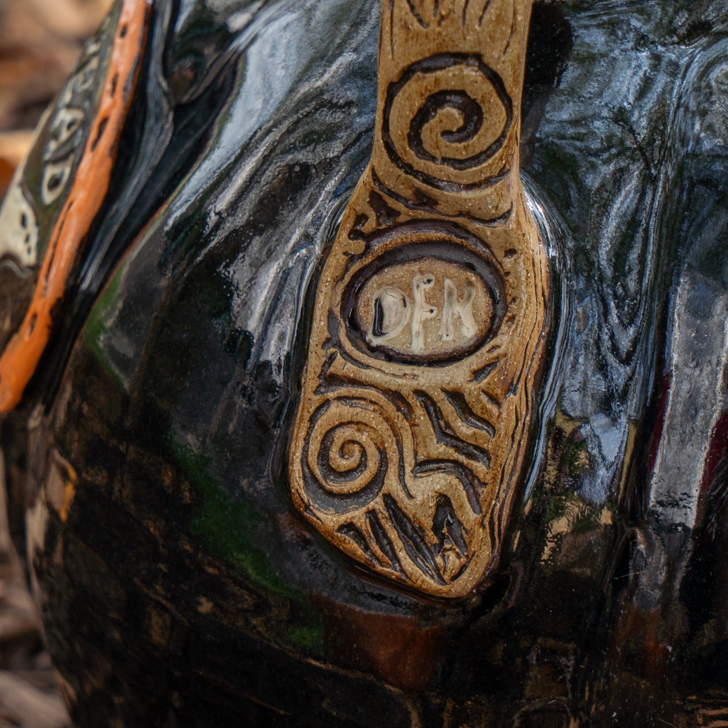 A close-up of the Blk Punkin Growler by Romanick Pottery—a glossy black piece with an engraved vertical handle reading DEN, accented by decorative carvings and handmade-inspired patterns.