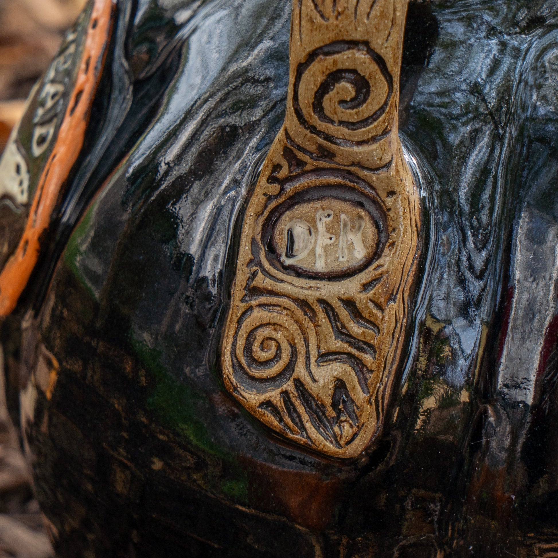 A close-up of the Blk Punkin Growler by Romanick Pottery—a glossy black piece with an engraved vertical handle reading DEN, accented by decorative carvings and handmade-inspired patterns.