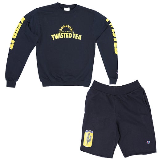 A matching dark blue Champion loungewear set consisting of a crewneck sweatshirt and shorts, displayed against a white background. The sweatshirt has yellow "TWISTED TEA HARD ICED TEA" branding with a sunburst on the chest, and "KEEP IT" vertically on the left sleeve and "TWISTED" vertically on the right sleeve. The shorts feature a yellow Twisted Tea can graphic on the lower left leg. Both garments have small Champion logos visible.