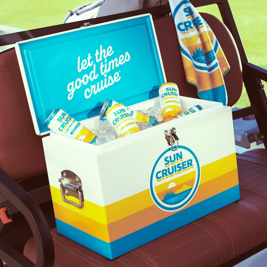 Sun Cruiser hard cooler with classic coloring and "Let the good times cruise" styled on the inner lid. Cooler is sitting on a golf cart seat with a Sun Cruiser golf towel