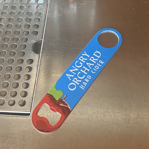 This blue paddle opener has the writing "Angry Orchard Hard Cider" in the center. On one end is a red apple which cuts open for the opener.