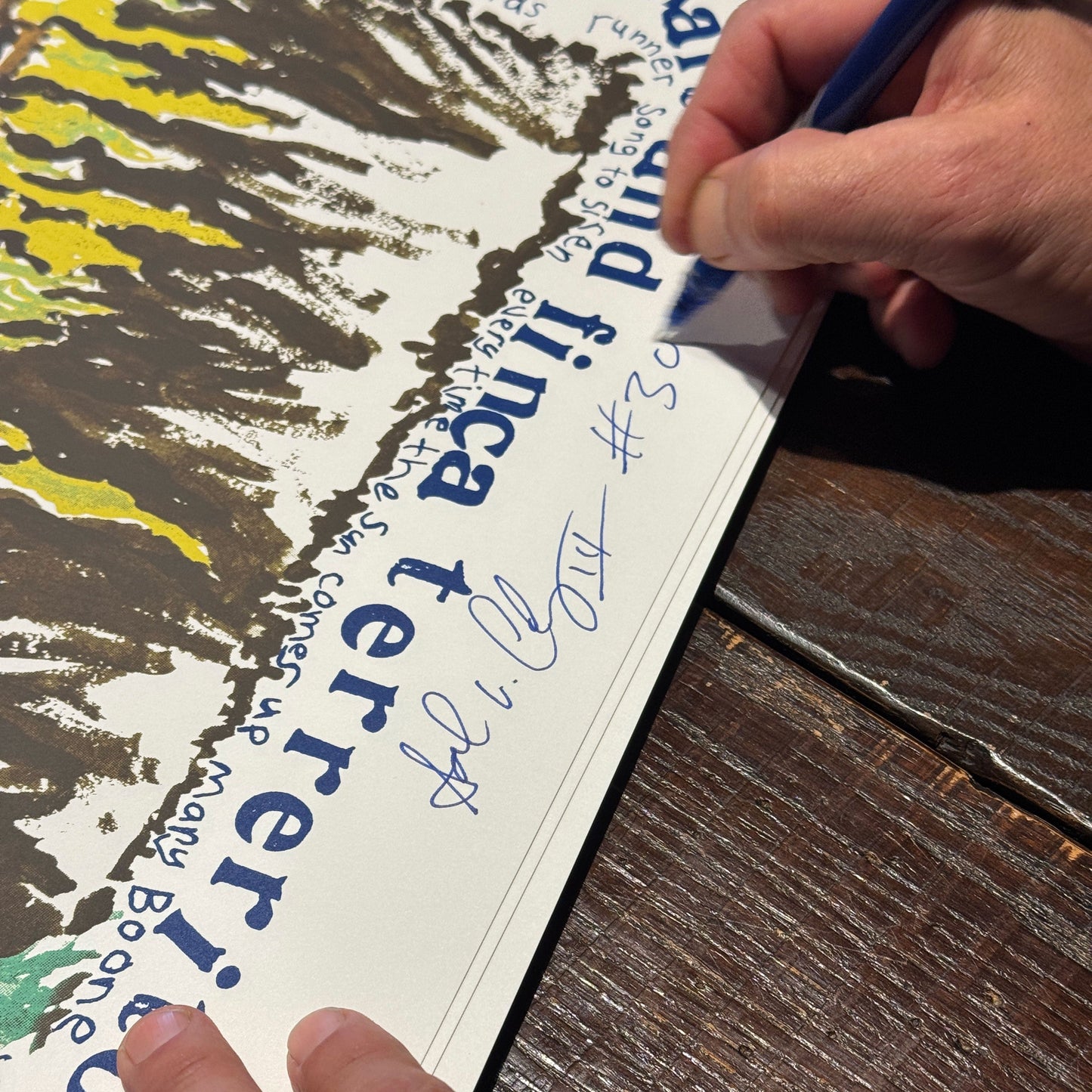 Person signing a poster with a pen on a wooden surface