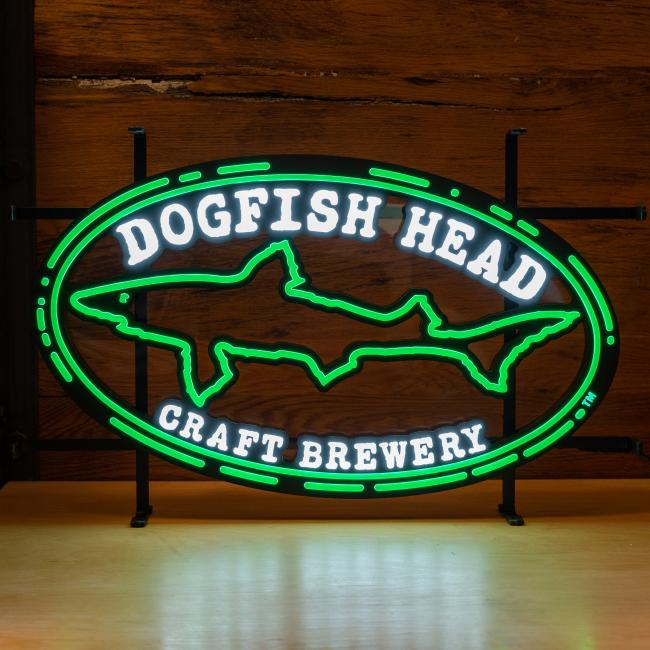 The Merchtank Craft Brewery Logo LED Neon features a green outlined shark and "Dogfish Head Craft Brewery" in white, displayed on wood, with durable LED lighting for lasting brightness.