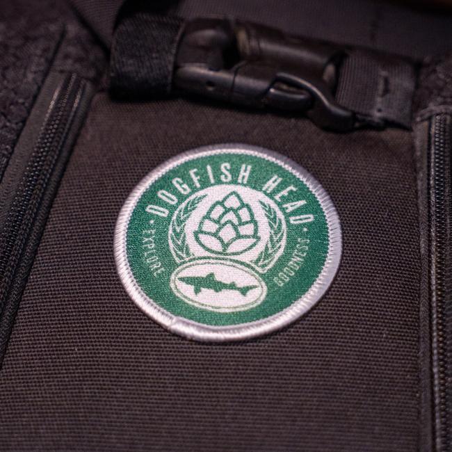 The GRAFFITI INC Explore Goodness Patch features a circular hop design with green accents, sewn onto black fabric—ideal for backpacks or jackets. Perfect for those who explore goodness in every sip.
