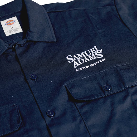 A navy Dickies button-up work shirt with a pocket on each side of the chest. Also features the Samuel Adams logo embroidered over the left side pocket.