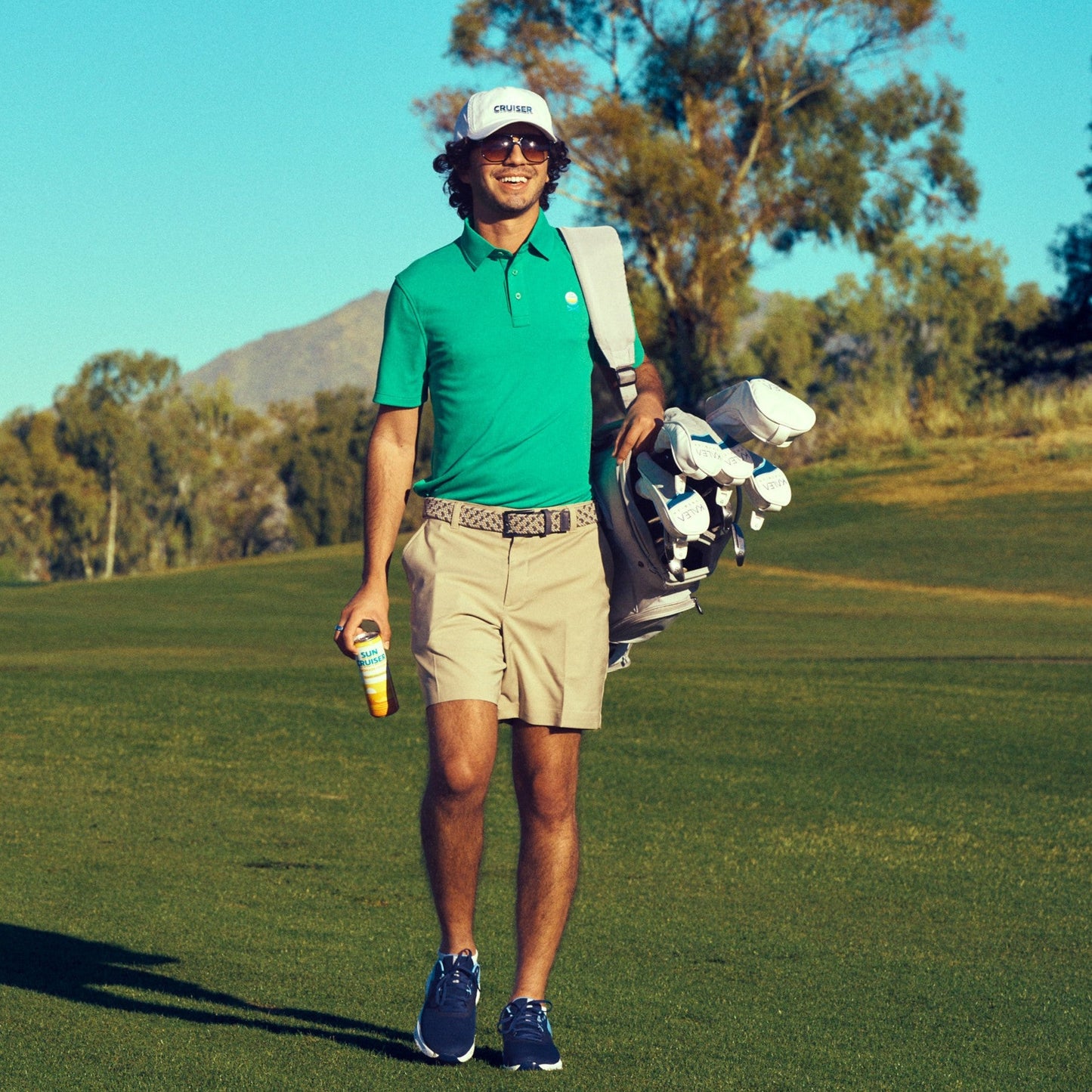Man in green shirt and khaki shorts carrying a golf bag on a golf course