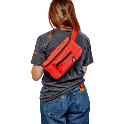 Woman wearing the red Angry Orchard belt bag. The bag has two pockets with a small Angry Orchard apple on the smaller pocket, as well as an adjustable strap.