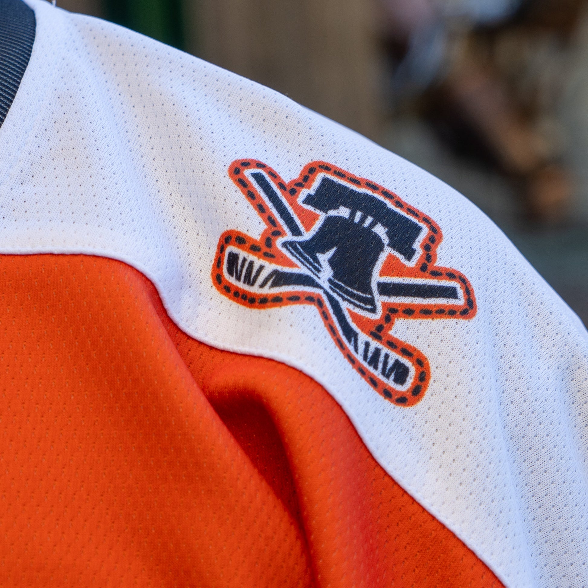 Close-up of the Dogfish Head x Garnet Hathaway Hockey Jersey by In Your Face Apparel, showing a shoulder patch with a stylized Liberty Bell and crossed hockey sticks in orange, black, and white—honoring first responders.