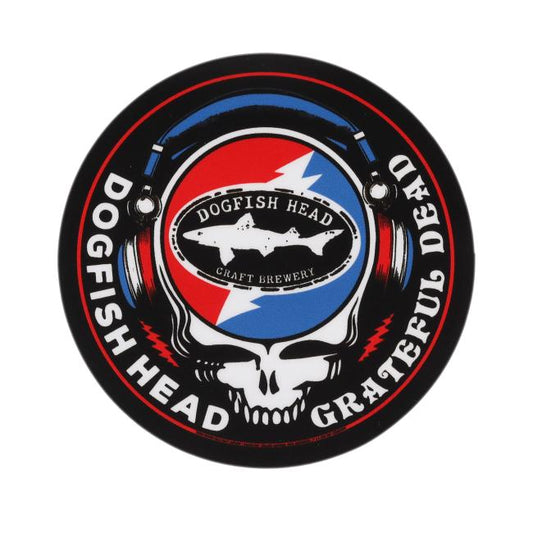 Black round sticker with "Dogfish Head" "Grateful Dead" written around the circle. White skull is featured in the center wearing blue and red headphones. In the head of the skull is a black Dogfish Head shark and shield logo with the background of a circle which is half red and half blue with a lightning bolt going through it.