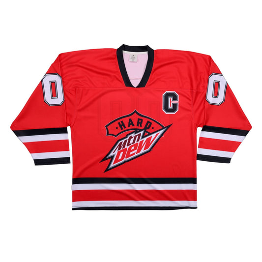 A vibrant red hockey jersey displayed flat, featuring a black V-neck collar. The front displays the 'Hard Mtn Dew' logo prominently in the center, with 'Hard' on a red banner above the white, red, and black Mtn Dew logo. A black 'C' is on the upper right chest, and the number '0' in white with a black outline is on both shoulders. Black and white stripes adorn the forearms.