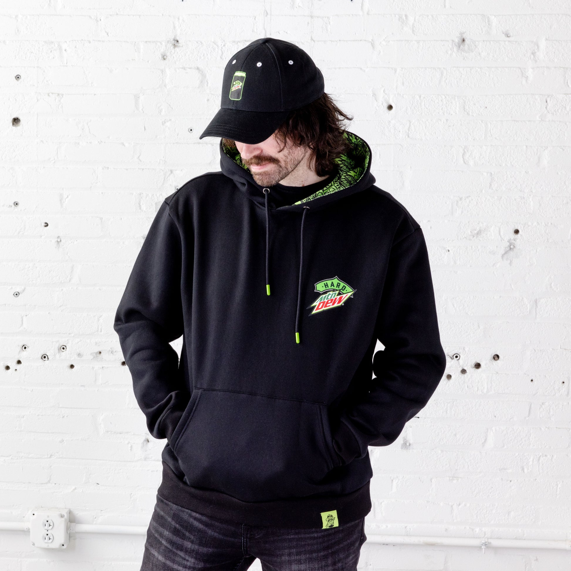 Model looking down wearing a relaxed fit baseball hat with embroidered Hard Mountain Dew can logo in neon green and black hat.