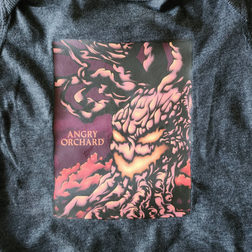 Front of black onesie with image of "haunted tree" and writing "Angry Orchard". Tree is made to look like it has a face - like a jack-o-lantern. 