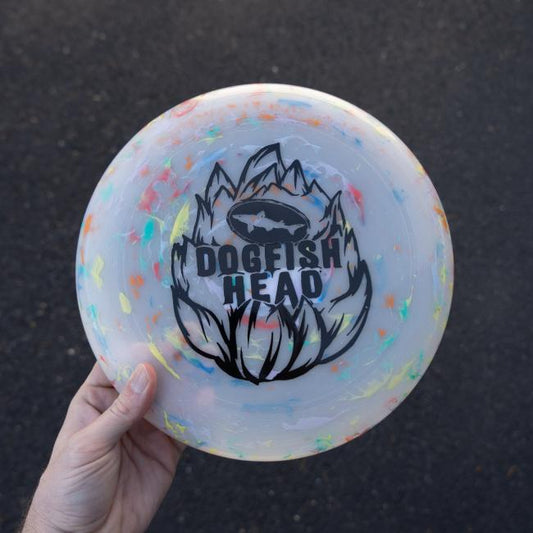 A hand holds the Hop Design Frisbee by Arrasmith Promotions LLC—featuring colorful splatters and a hop outline design—set against a dark asphalt background.