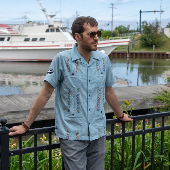 The front of the shirt features a button pocket on each side of the chest as well as directly below on the bottom of the shirt. Dogfish Head shark and shield logo is stitched on the bottom of the left sleeve. Throughout the shirt featured is a blue and yellow spiral stitch, a dusty orange zigzag, and blue stripes.