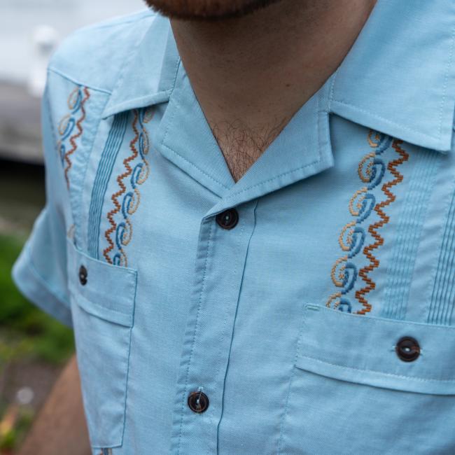 Close up of the stitching detail on the front of the shirt. Featured is a blue and yellow spiral stitch, a dusty orange zigzag, and blue stripes.