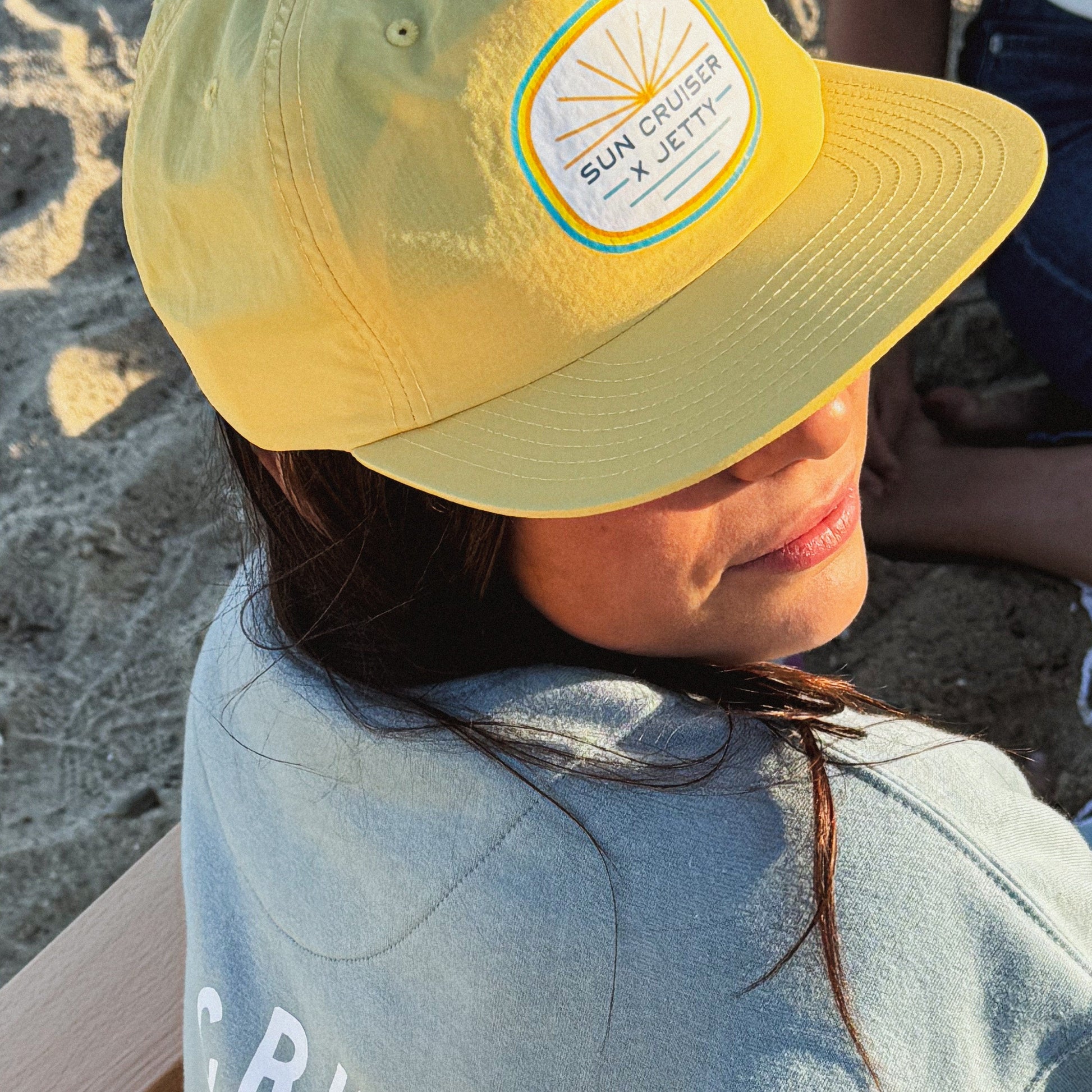 Person wearing a yellow cap with branding on a sandy background