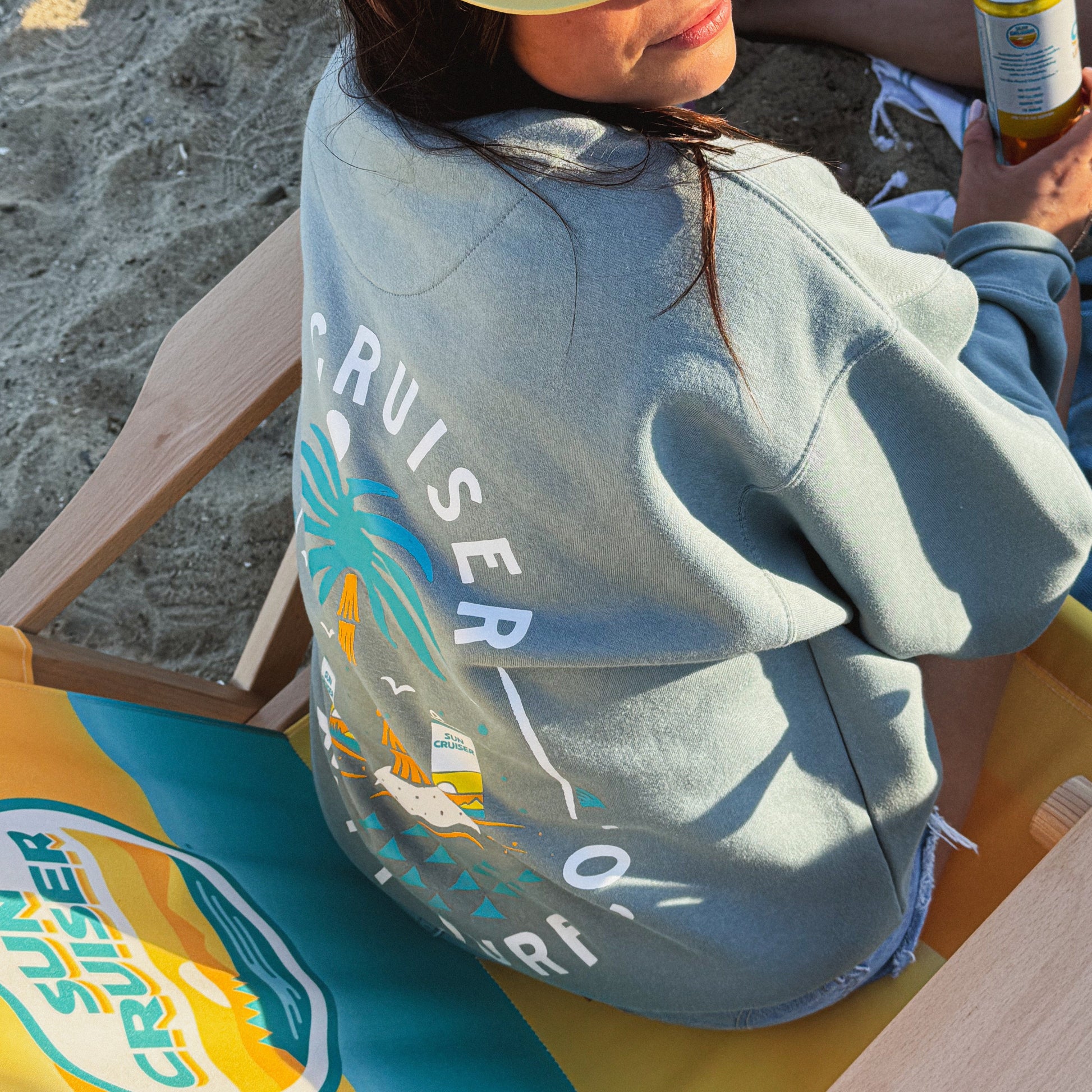 Person wearing a blue sweatshirt with 'Sun Cruiser' branding on a beach.
