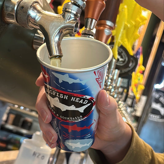 Bartender pouring draft beer from tap into Dogfish Head aluminum can glass, reusable pint cup with shark logo design at brewery bar station