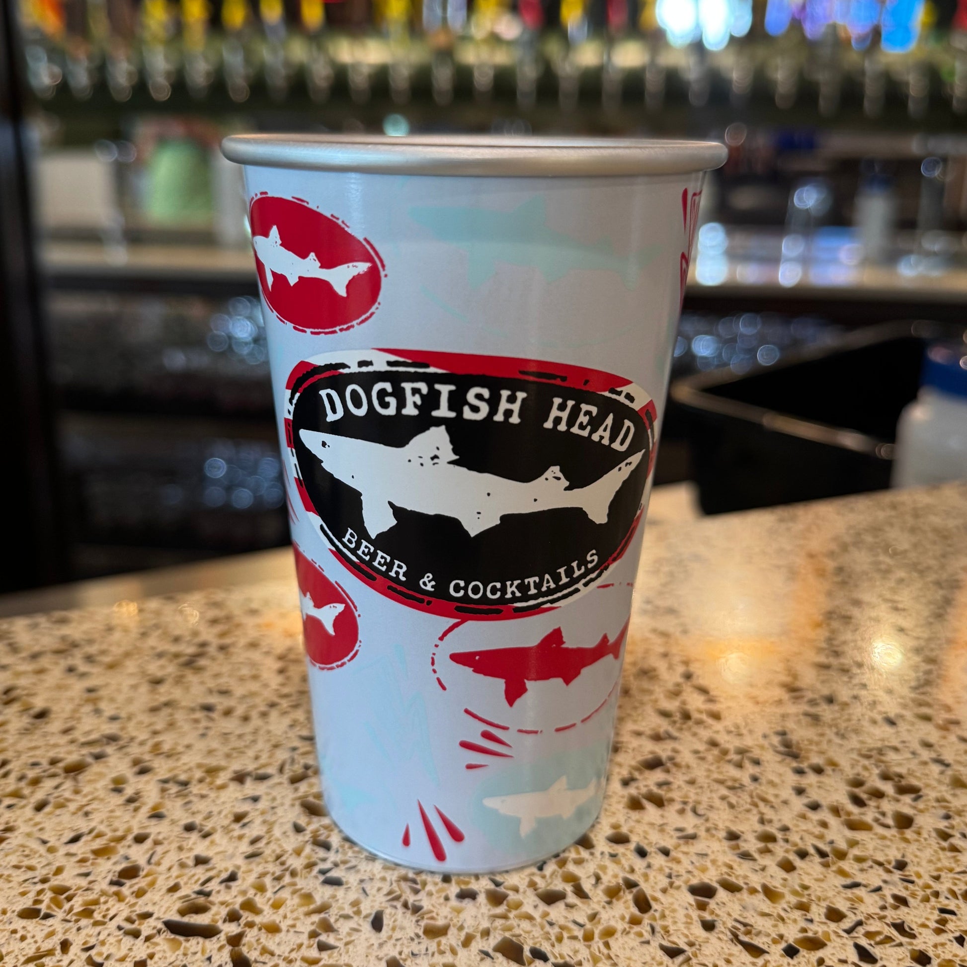 Dogfish Head aluminum can style reusable pint glass with shark logo design, lightweight eco-friendly drinkware on bar counter in taproom setting