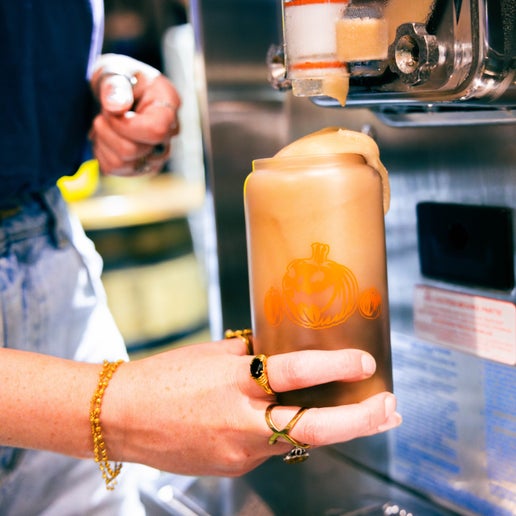 Color changing can glass features imagery of orange pumpkin on the front with a smaller one on both sides of the larger. Glass is pictured being filled with a drink.