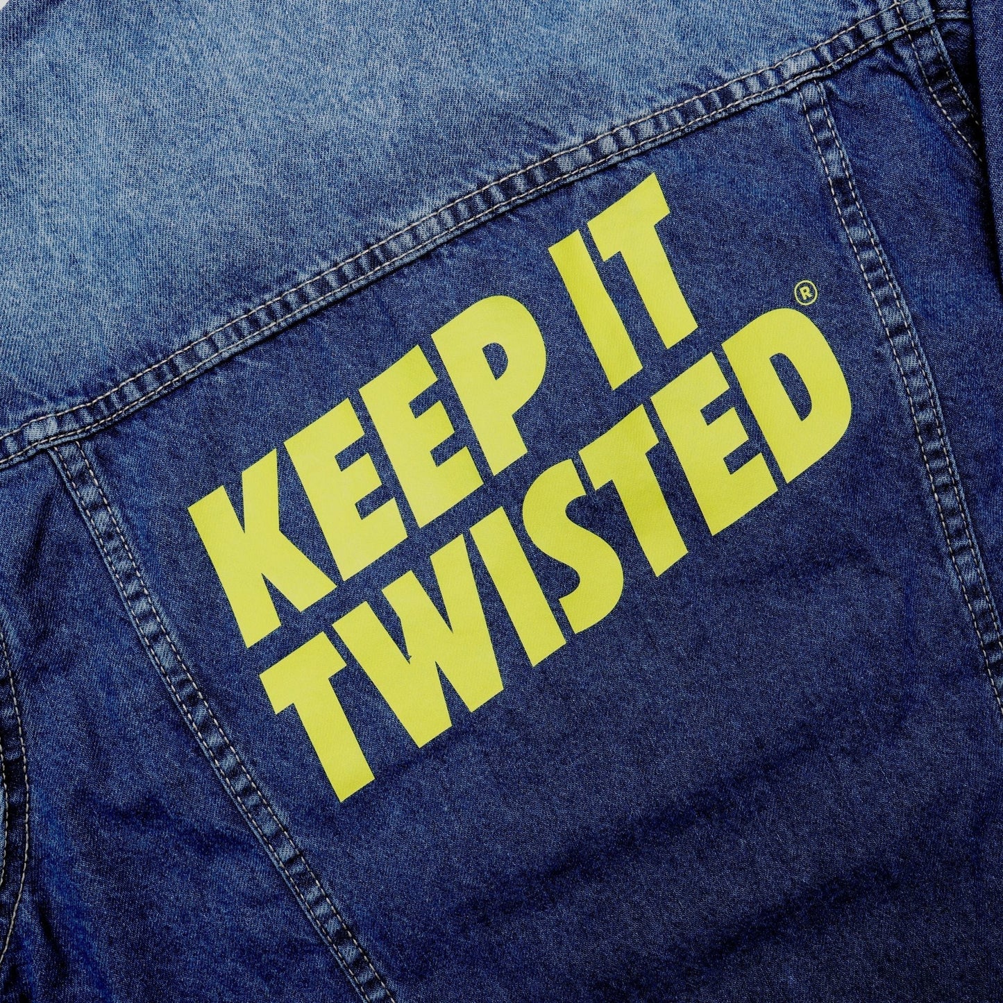 Blue denim jacket with 'KEEP IT TWISTED' text in yellow on a close-up view.