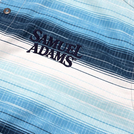 Close up views of a Samuel Adams KUHL Blue Stripe Ikonik Persuadr Short Sleeve Button Up, featuring horizontal blue-toned stripes, snap buttons, and embroidered Samuel Adams logo on the left chest.