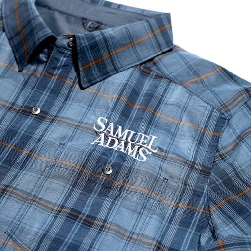 Close up of white Samuel Adams logo on the left chest of a  Blue, grey, and brown flannel style jacket 