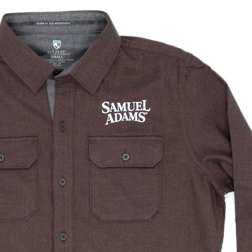 The KUHL Brown Descendr Flannel features securable chest pockets, an interior security pocket, 2-button adjustable cuffs, and a white Samuel Adams logo above the left side chest pocket.