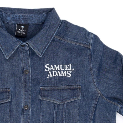 The KUHL super lightweight performance denim button-up shirt features a snap front, two front chest pockets, Princess seams, and the Samuel Adams logo embroidered over the left side chest pocket in white.