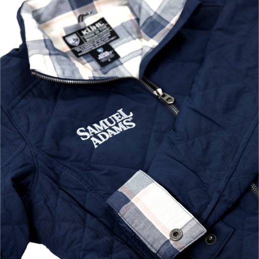 Our KUHL W Indigo Stunnr Insulated Jacket has features like a cozy flannel lining, zippered hand warmer pockets, an internal security pocket, and the Samuel Adams logo embroidered in white on the right side of the upper chest..