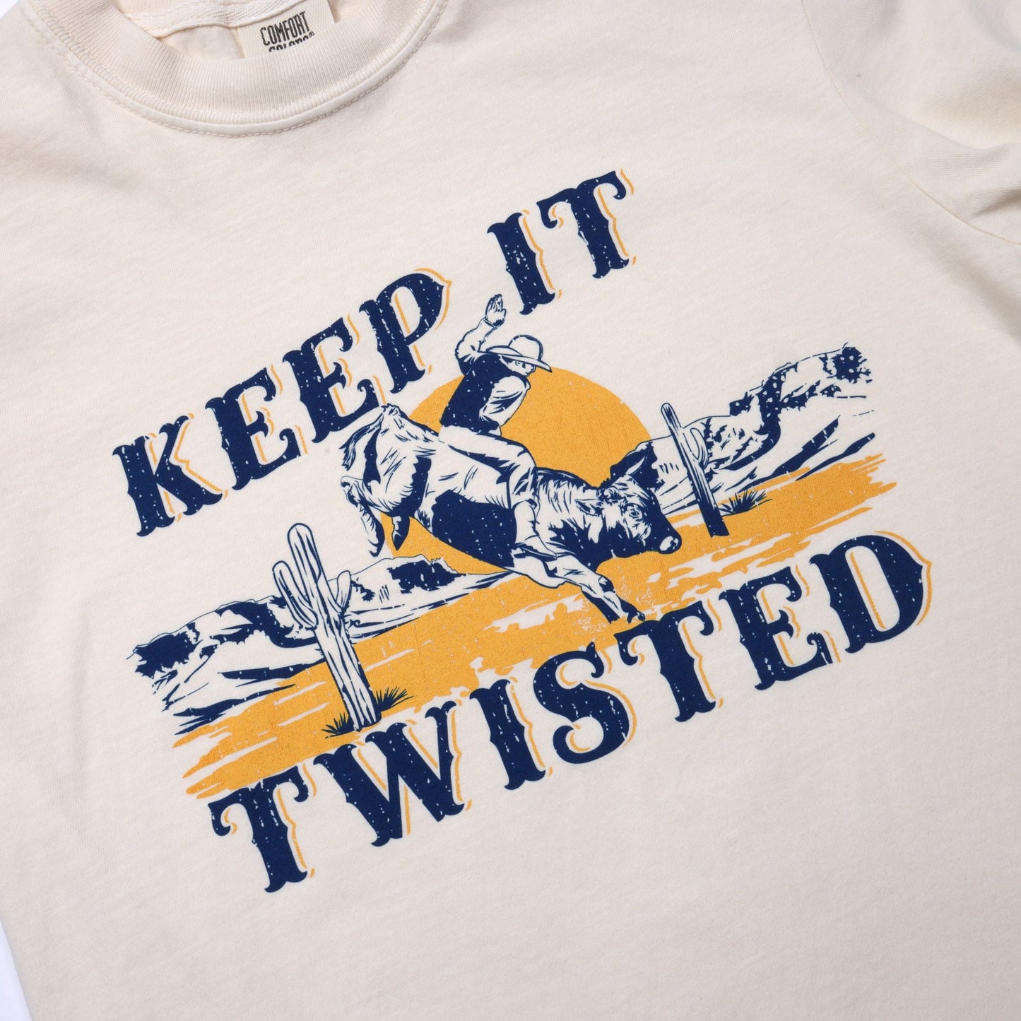 Tee shirt with graphic design of a person riding a bull and text 'Keep It Twisted' on a beige background.