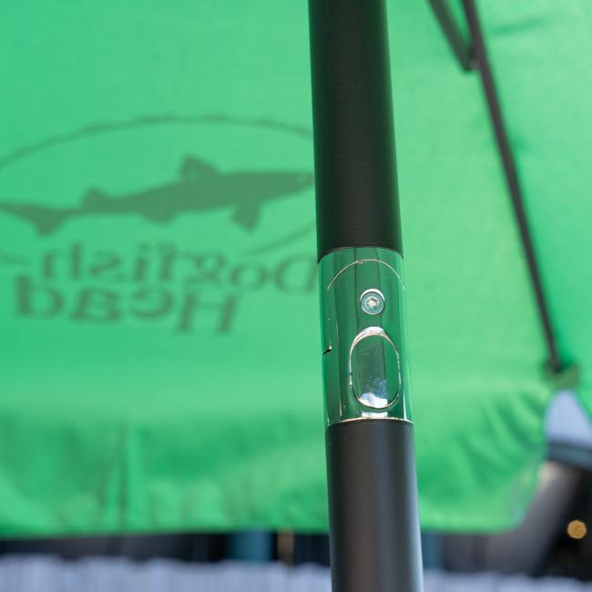 Close-up of a black pole with a shiny metallic connector in front of an outdoor Lg Logo Umbrella from Steamboat Marketing Inc, featuring sun protection and green fabric with visible logo printing.