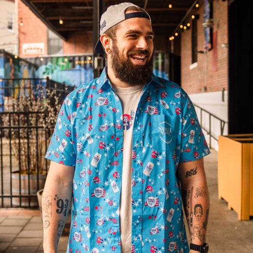 Front view of a light blue short sleeve button-up shirt with an all-over red, white, and blue Samuel Adams American Light print.