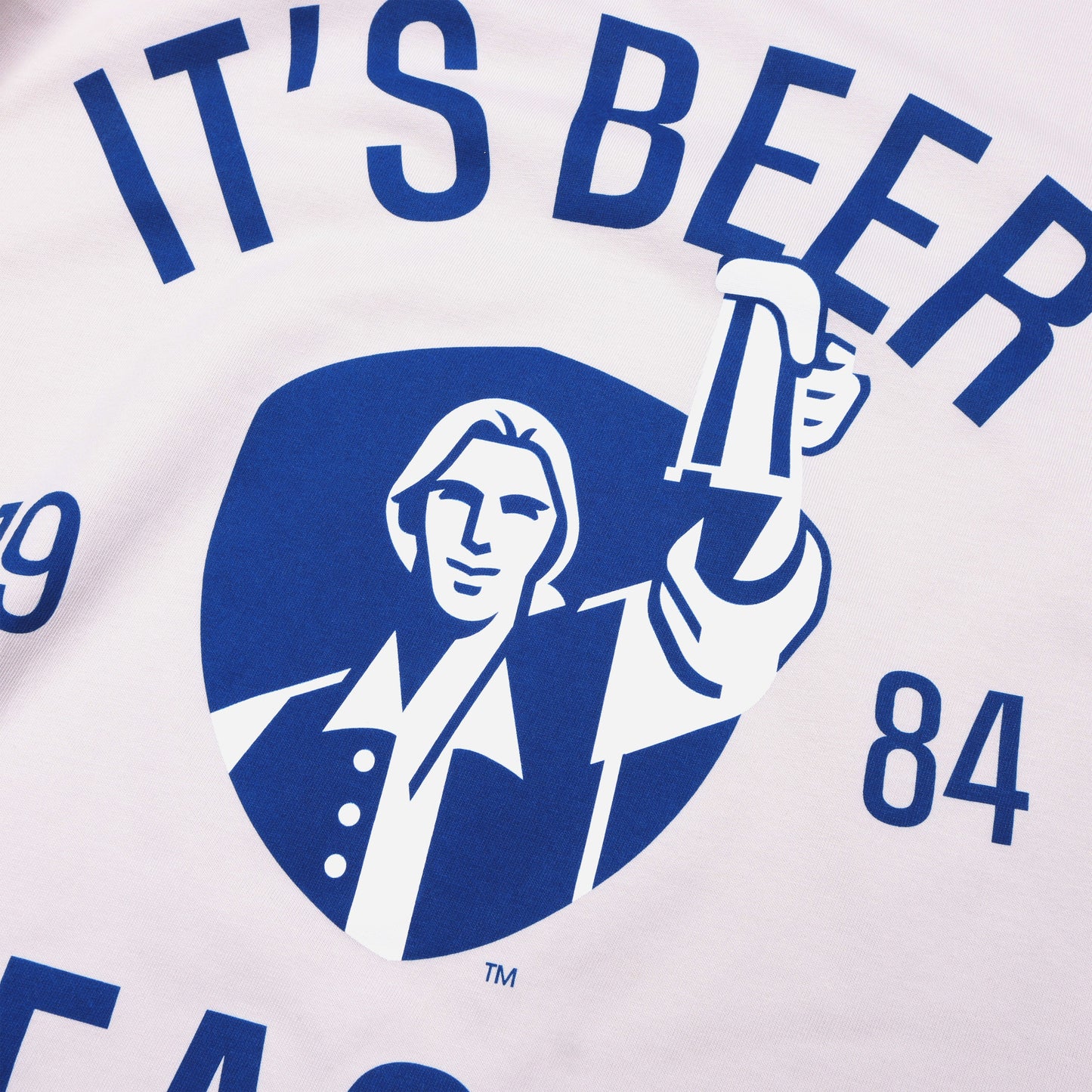 Close-up of imagery on the front of tee, features blue writing "It's Beer Season", "Samuel Adams", "1984", and imagery of Sam Adams hoisting a stein on a blue shield background.