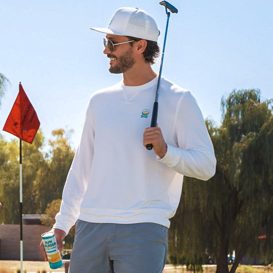 Man in white shirt and gray pants holding a golf club on a golf course with trees and blue sky in the background.