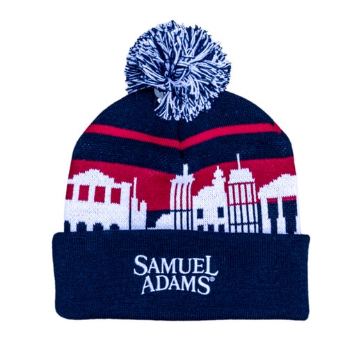 Beanie with a blue base and red stripes, pom on top is blue and white. A white Boston skyline is wrapped around the beanie. On the fold over the Samuel Adams logo is featured in white.