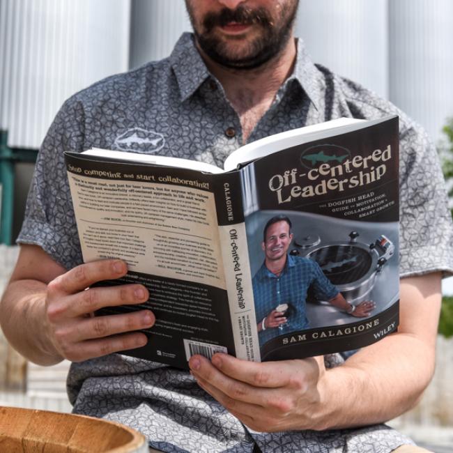 Outdoors, a person in a patterned short-sleeve shirt reads Book- Off-Cent Leadership by J Wiley and Sons Publishing, showing both the front and back covers.