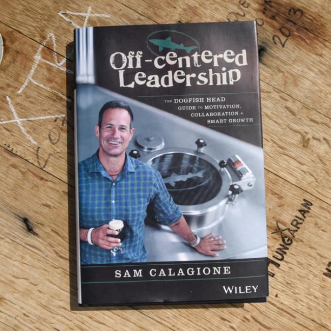 Book-Off-Cent Leadership by J Wiley and Sons Publishing rests on a wooden surface. The cover features Sam smiling with beer and brewing gear, symbolizing creative leadership and collaboration in business.