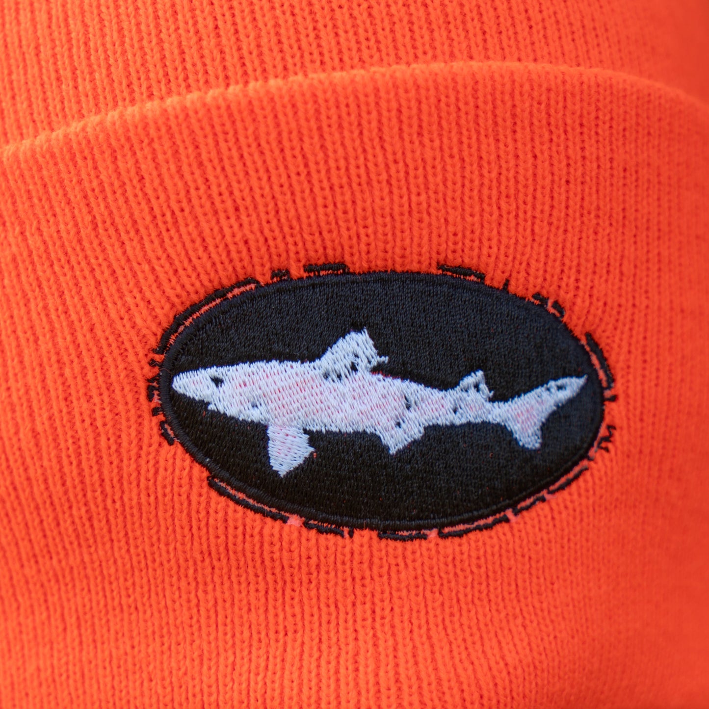 Close-up of the Orange Beanie by Mirror Image Inc., showcasing a warm orange knit with a black oval patch featuring a white shark design stitched at the center.