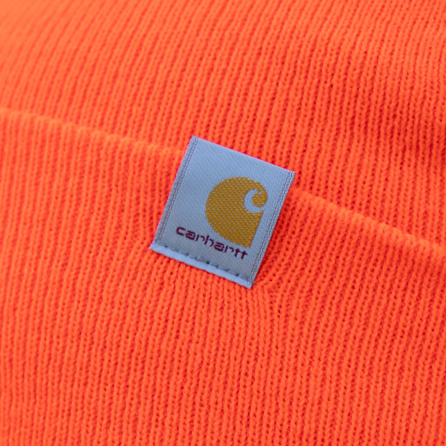 Close-up of a warm orange knit fabric Orange Beanie by Mirror Image Inc., featuring a square logo patch.